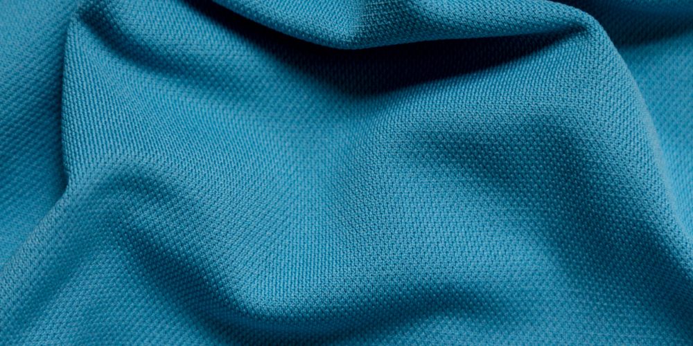 A full frame image of bright blue polyester fabric that is wrinkled. The material is simply composed with shadows below the ripples in the material.  The fabric is used for wicking sports applications.